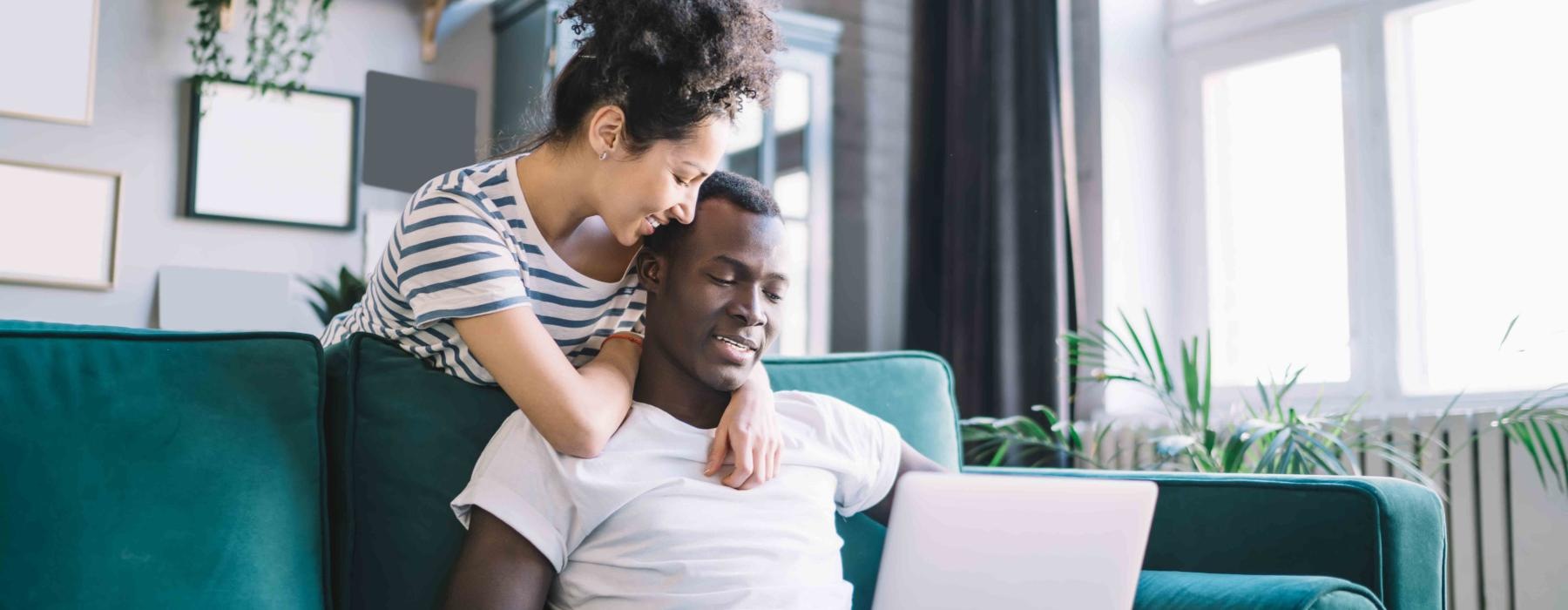 a man and a woman sitting on a couch looking at a laptop